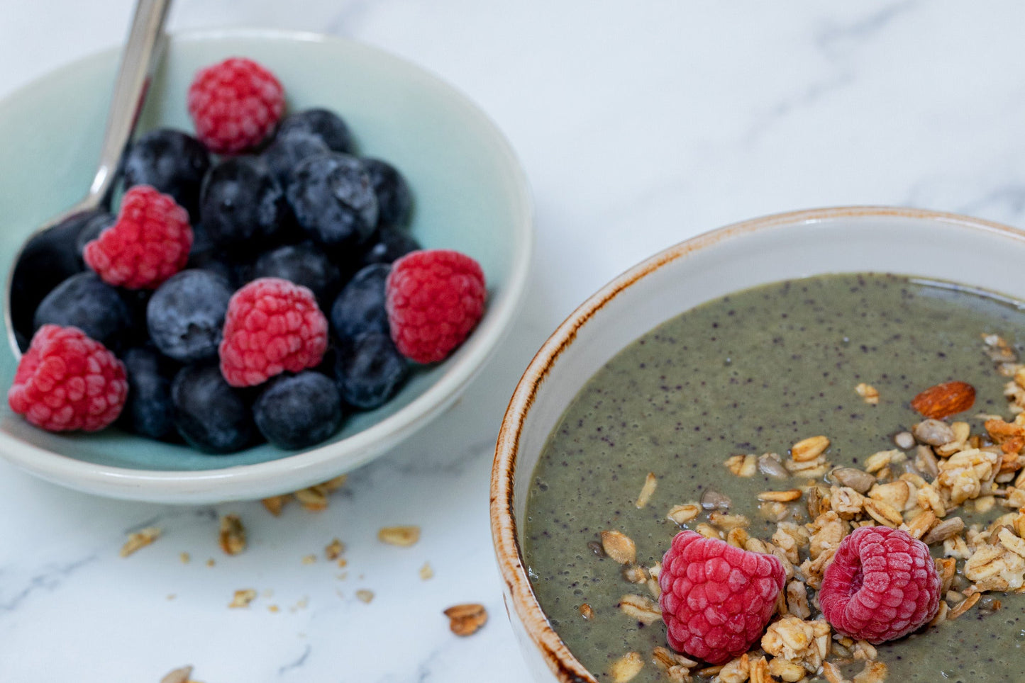 A bowl of oatmeal with blueberries and raspberries on a marble surface. A side of cereal flakes is also visible.